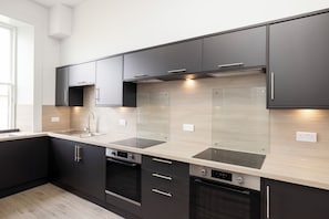 A modern kitchen with dark cabinetry, stainless steel appliances, and a light wood backsplash. - Spacious City-Centre Home with Garden (Edinburgh)