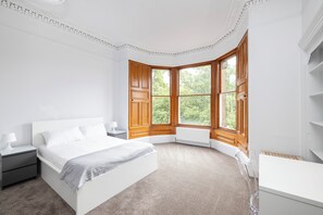 A bedroom with a large window, a bed, a nightstand, and a desk. - Spacious City-Centre Home with Garden (Edinburgh)