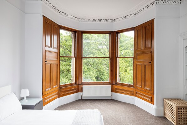 A corner bedroom with a bay window, a radiator, a bed, and a nightstand. - Spacious City-Centre Home with Garden (Edinburgh)