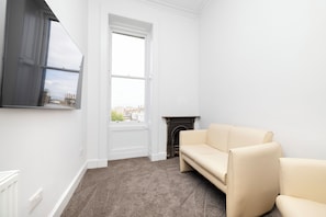 A room with a beige sofa, a fireplace, a large window, and a carpeted floor. - Spacious City-Centre Home with Garden (Edinburgh)