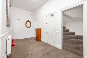A hallway with carpeted flooring, white walls, a wooden dresser, a fire extinguisher, and a staircase. - Spacious City-Centre Home with Garden (Edinburgh)