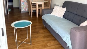 Ein Wohnzimmer mit grauem Sofa, einem runden Couchtisch, einem Esstisch mit Korbstühlen und farbenfrohem Blumenpapier.