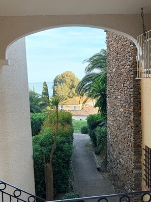 A corridor with a stone wall, a metal railing, and a view of a building and trees. - CAP ESTEREL Studio (Saint-Raphaël)
