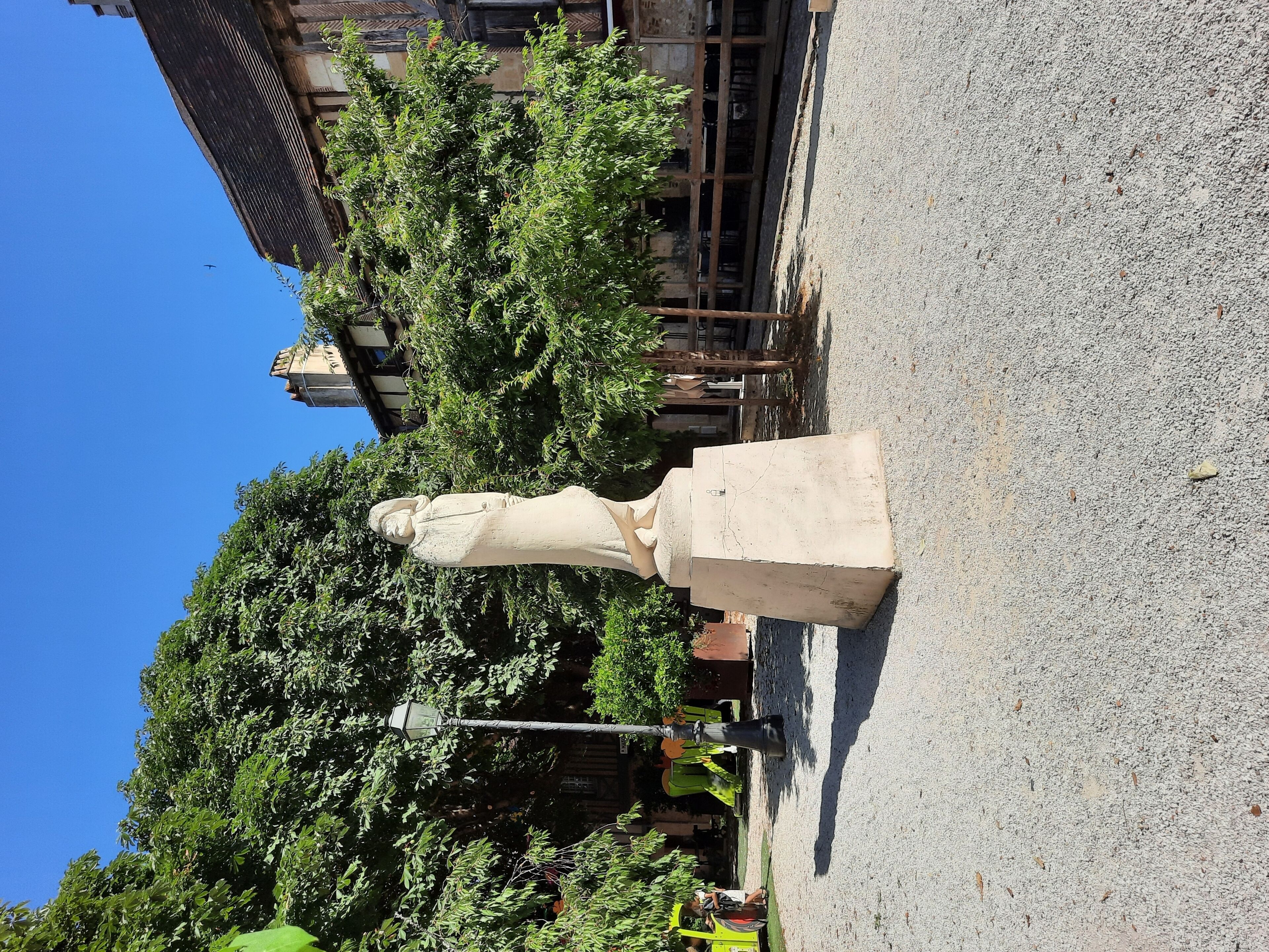 A statue in a courtyard with trees and a building in the background.