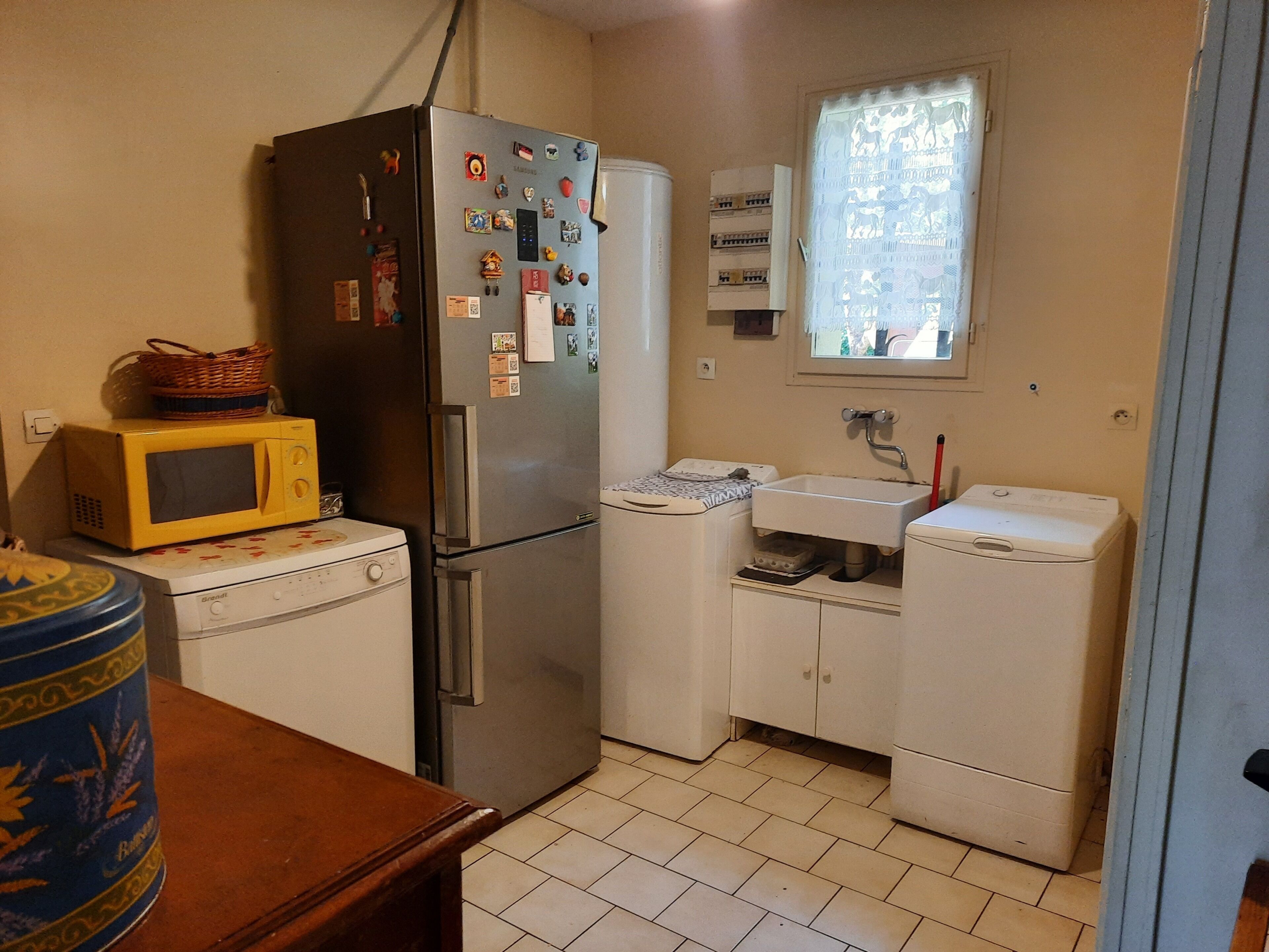 A compact kitchen with a refrigerator, microwave, washing machine, and a small sink.