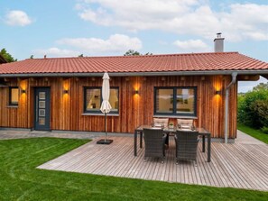 Et træhus med rødt tegltag, en terrasse med udendørs møbler og en velplejet græsplæne.