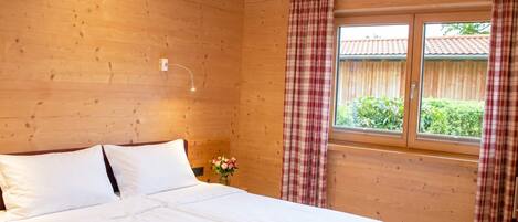 A wooden cabin bedroom with a bed, curtains, a window, and a nightlight.