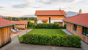 Une maison moderne avec un toit recouvert de tuiles rouges, une pelouse bien entretenue et une terrasse dallée.