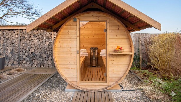Un sauna en bois doté d’un toit incurvé, d’un banc en bois à l’intérieur et d’une étagère avec des fruits à l’extérieur.