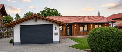 A modern house with a garage, a well-maintained lawn, and a large bush.