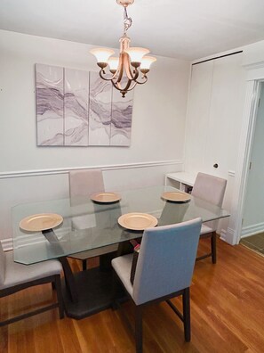 Een eethoek met een glazen tafel, zes stoelen, een kroonluchter en een marmeren kunstwerk aan de wand.