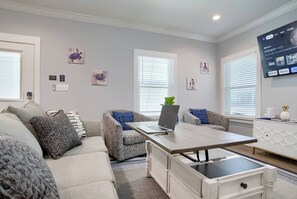 Ein Wohnzimmer mit einer Couch, einem Couchtisch mit einem Laptop, einem an der Wand montierten Fernseher und einer Wand mit Kunstwerken.