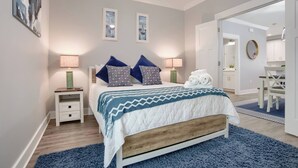 Un dormitorio con cama, mesitas de noche, un espejo y un baño visible a través de una puerta abierta.