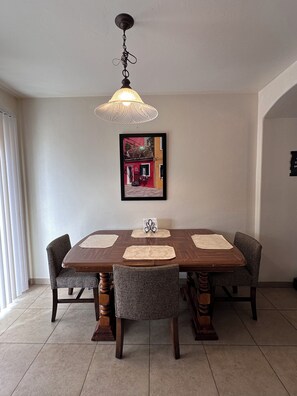 Un comedor con una mesa de madera, cuatro sillas, una lámpara colgante y un cuadro en la pared.