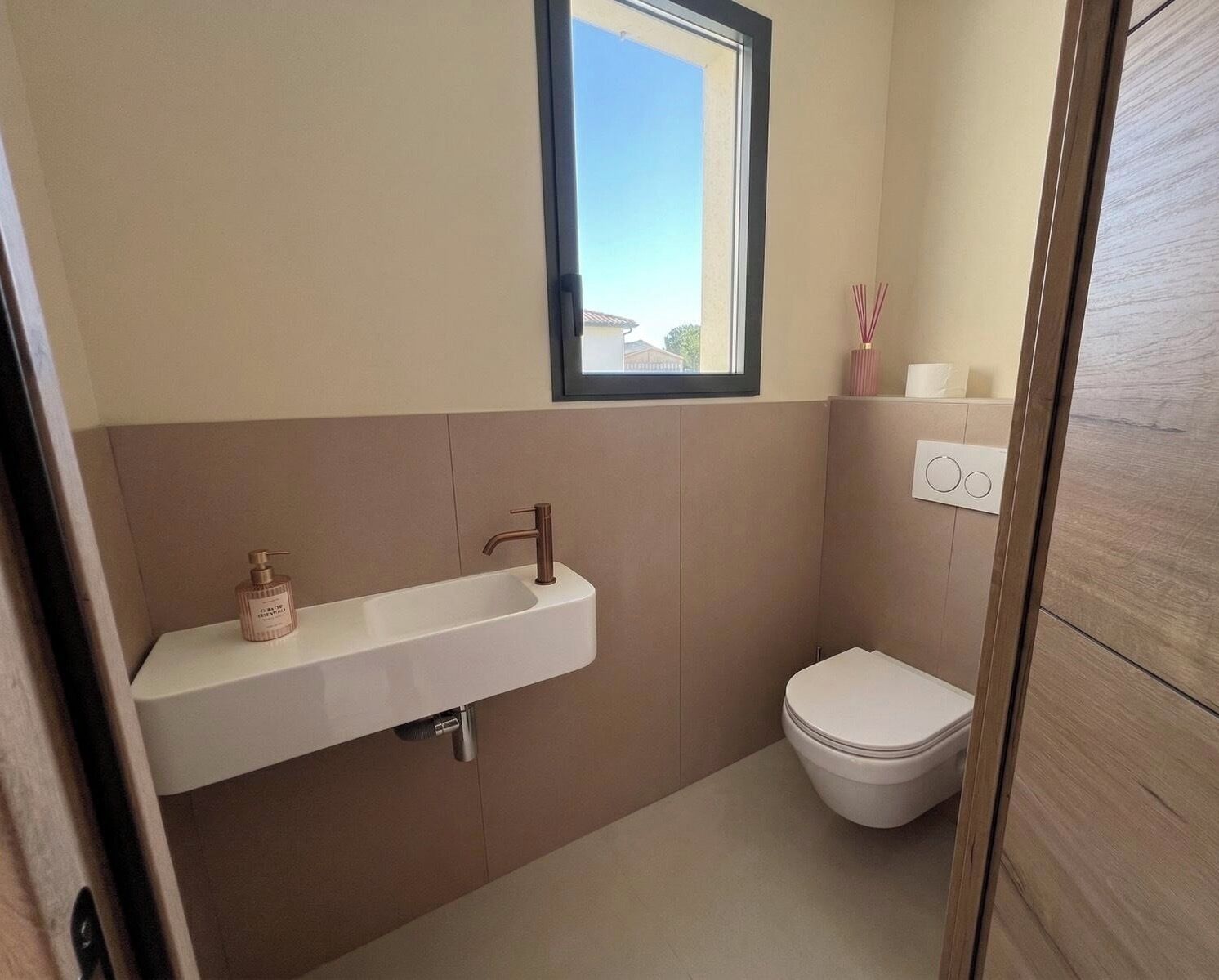 Une salle de bain avec un lavabo blanc, des toilettes et une fenêtre.