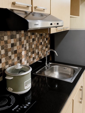 A kitchen with a modern stove, a sink, and a slow cooker. - Cabina Baguio | Cozy Studio Near Session Road w/ Gym & Sauna (Baguio)