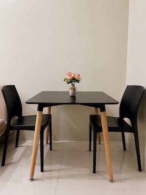 Una mesa de comedor con dos sillas, un florero con flores y una pared lisa.
