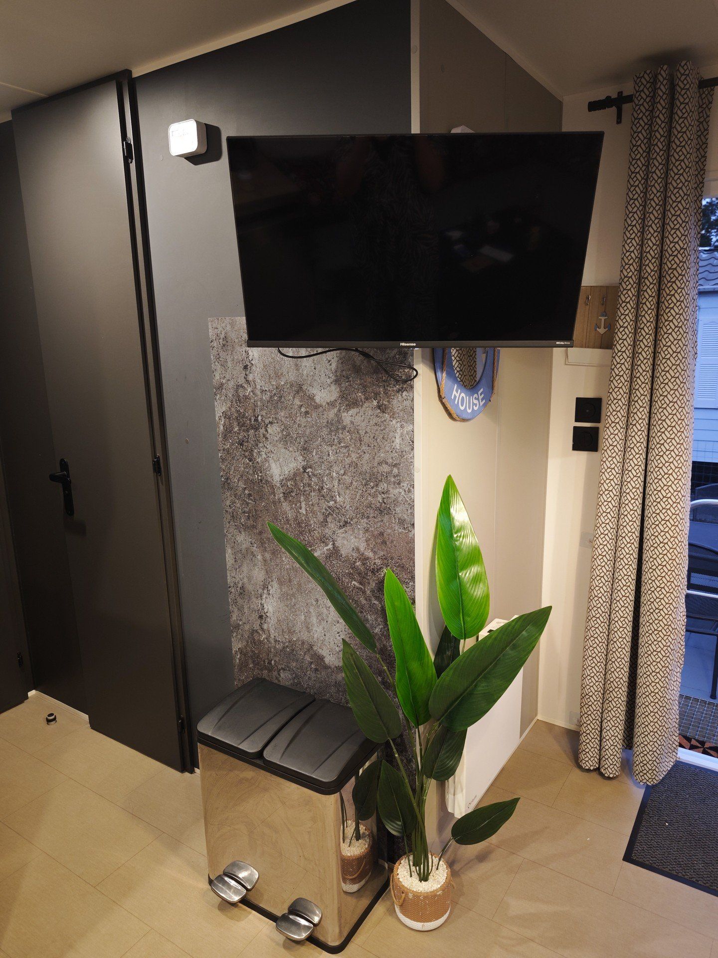 Een moderne woonkamer met een flatscreen televisie aan de muur, een klein bankje en een potplant.