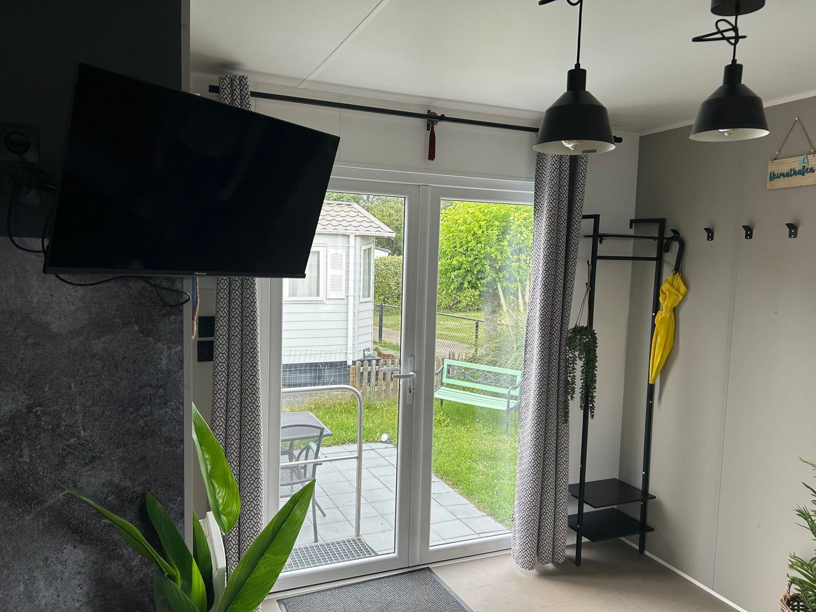 Une pièce avec un téléviseur, un banc à l’extérieur et une porte donnant sur un patio.