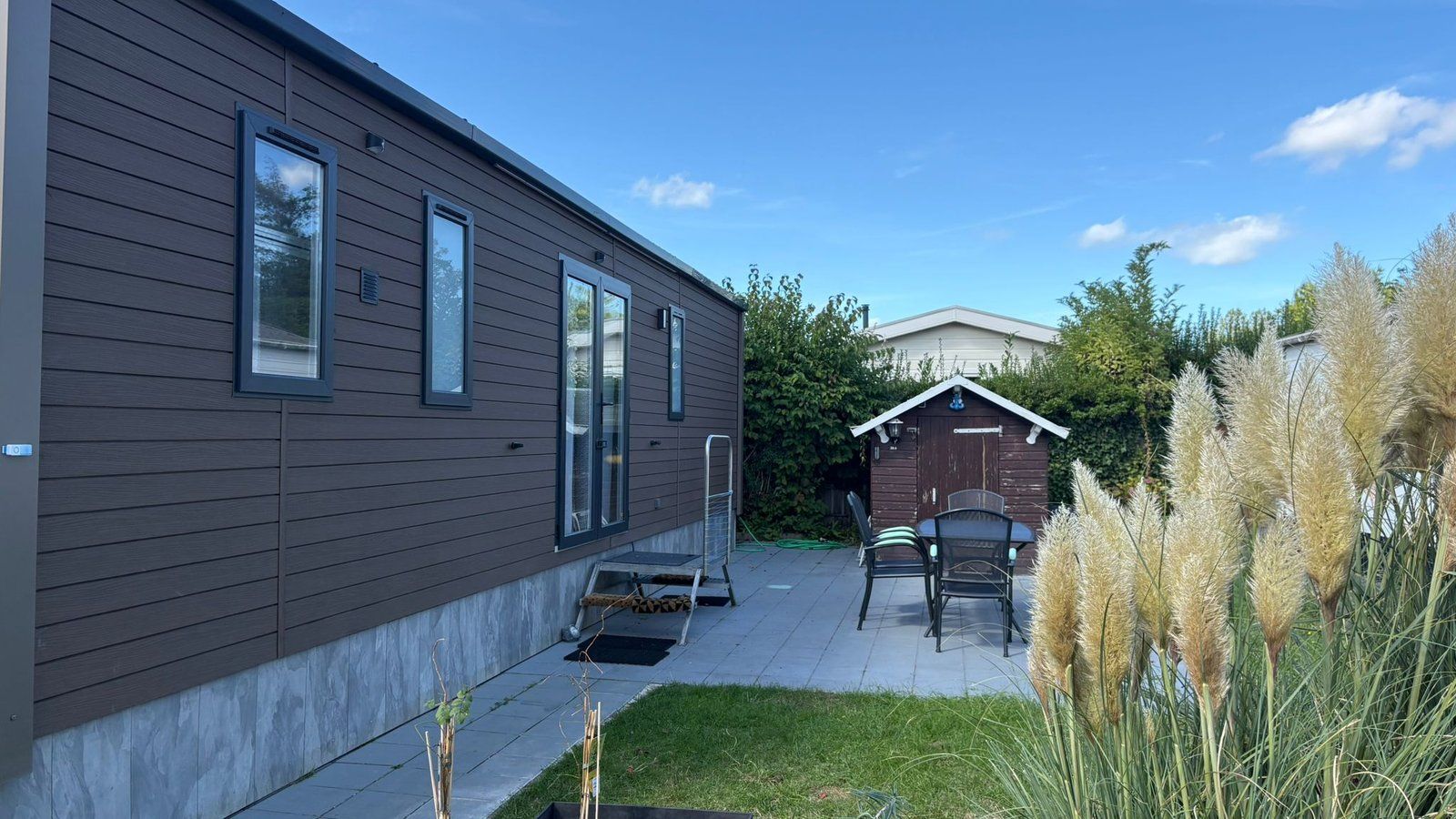 A modern house with a patio, a small shed, and a lawn.
