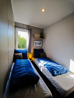 Ein Schlafzimmer mit zwei Betten, einem Fenster, einem Regal mit einer Pflanze und einem Wandbild.