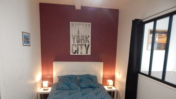 Une chambre à coucher avec un lit, deux tables de chevet, une affiche accrochée au mur et une fenêtre avec des rideaux.