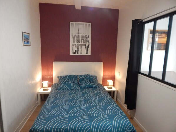 Quarto com uma cama, duas mesas de cabeceira, um cartaz na parede e uma janela com cortinas.