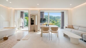 Una habitación de hotel moderna con un ventanal grande, una bañera, un comedor y un sofá.