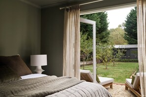 Ein Schlafzimmer mit Bett, Nachttischlampe und Blick auf einen Garten durch ein Fenster.