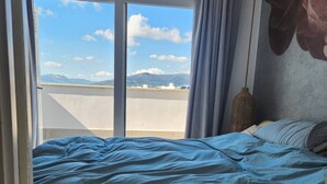 Ein Schlafzimmer mit Bett, Blick auf Berge durch ein Fenster und einer Pendelleuchte.