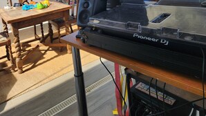 Ein Pioneer DJ-Turntable auf einem Holztisch in einem sonnendurchfluteten Raum mit großen Fenstern, einem blauen Sofa und einer Discokugel.