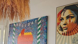Ein Zimmer mit einem großen abstrakten Gemälde, einem gerahmten Bild, einem Schreibtisch mit Computer und einer hängenden Leuchte.