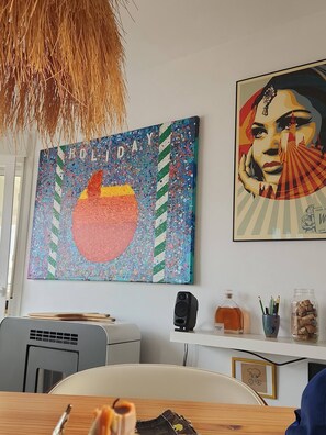 A room with a large abstract painting, a framed picture, a desk with a computer, and a hanging light fixture. - The Penthouse Tarifa - Artist's Residence Oasis (Tarifa)