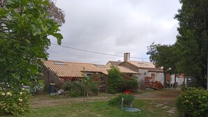A rustic house with a tiled roof, a stone wall, and a garden with various plants and a small tree. - A SWEET REST (Chauvé)