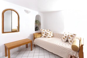 A bedroom with a bed, a bench, a mirror, and a shelf with a plant. - Folia Bianca-Coco & Belle (Imerovigli)