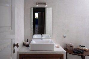 Ein Badezimmer mit einem rechteckigen Waschbecken, einem Spiegel darüber und Pflegeprodukten auf einem Holztischchen.