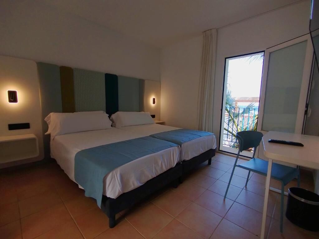 Una habitación de hotel con cama, mesitas de noche, una silla, un escritorio y vistas al exterior.