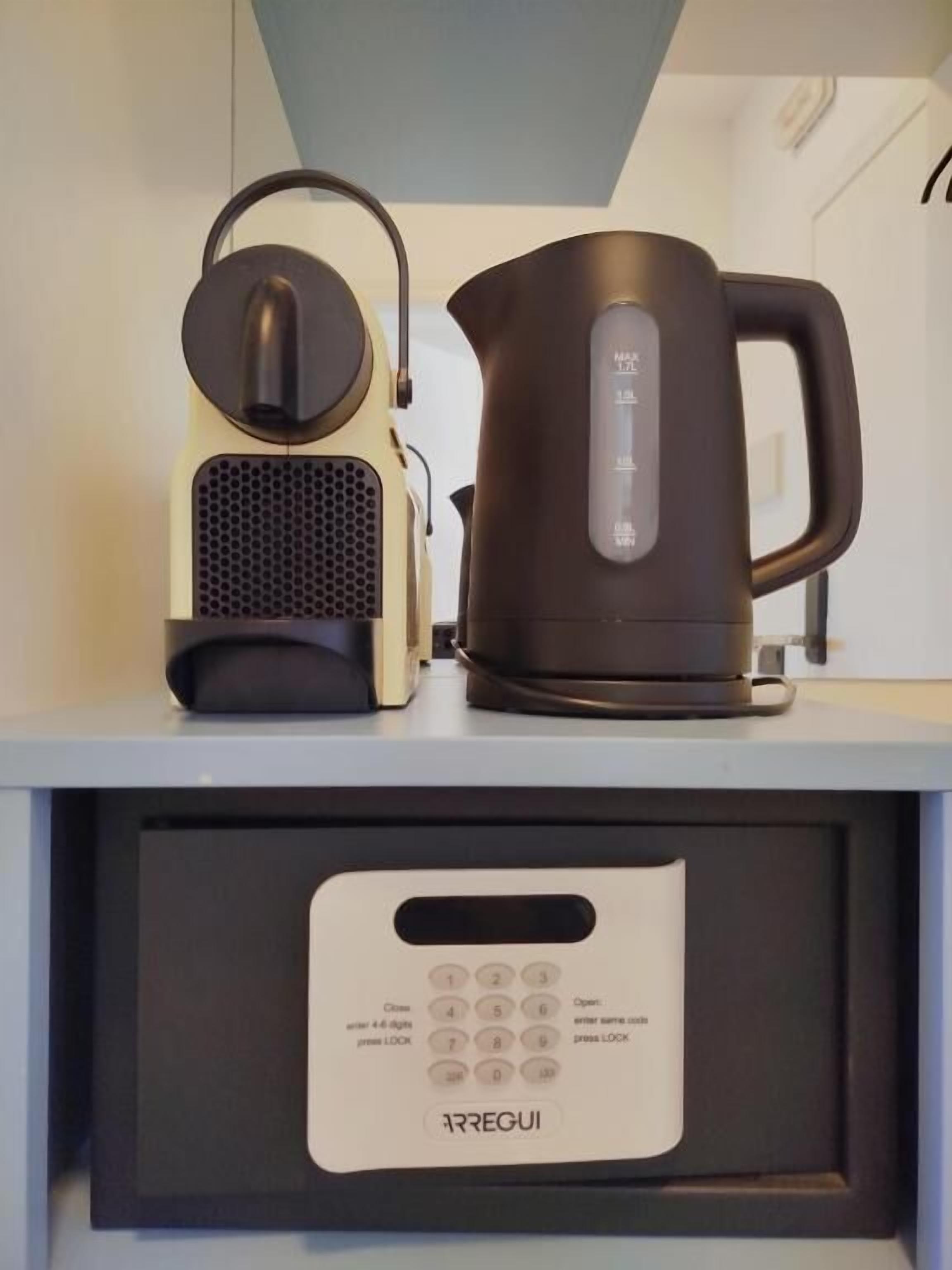 A kitchen area with a coffee maker, a kettle, and a control panel with buttons and a display.