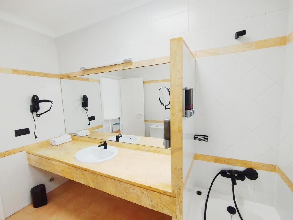 Un baño con tocador de madera, dos lavamanos, un espejo grande y zona de ducha.