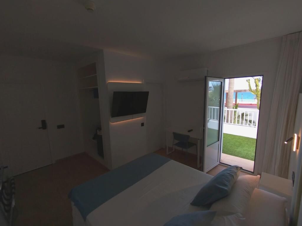 Habitación de hotel con cama, televisor montado en la pared, puerta corrediza de vidrio al exterior y una pequeña mesa.