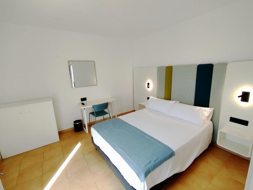 Habitación de hotel con cama, escritorio, silla y un pequeño cubo de basura.