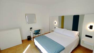 Habitación de hotel con cama, escritorio, silla y un pequeño cubo de basura.