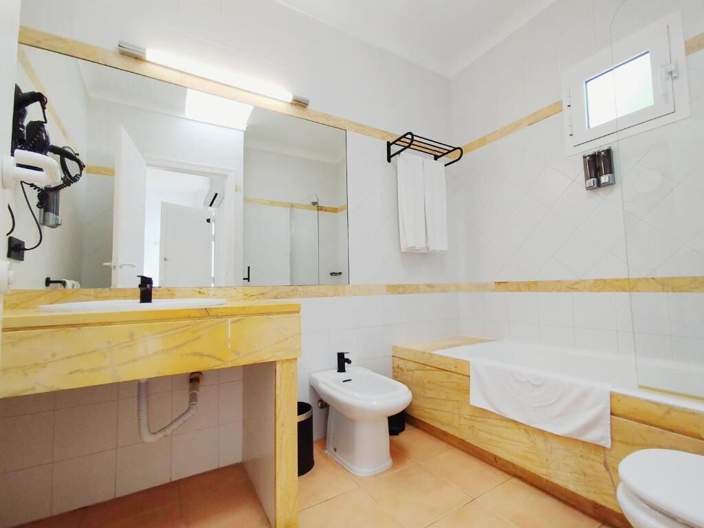 Een badkamer met een marmeren wastafel, een bidet, een bad en een grote spiegel.