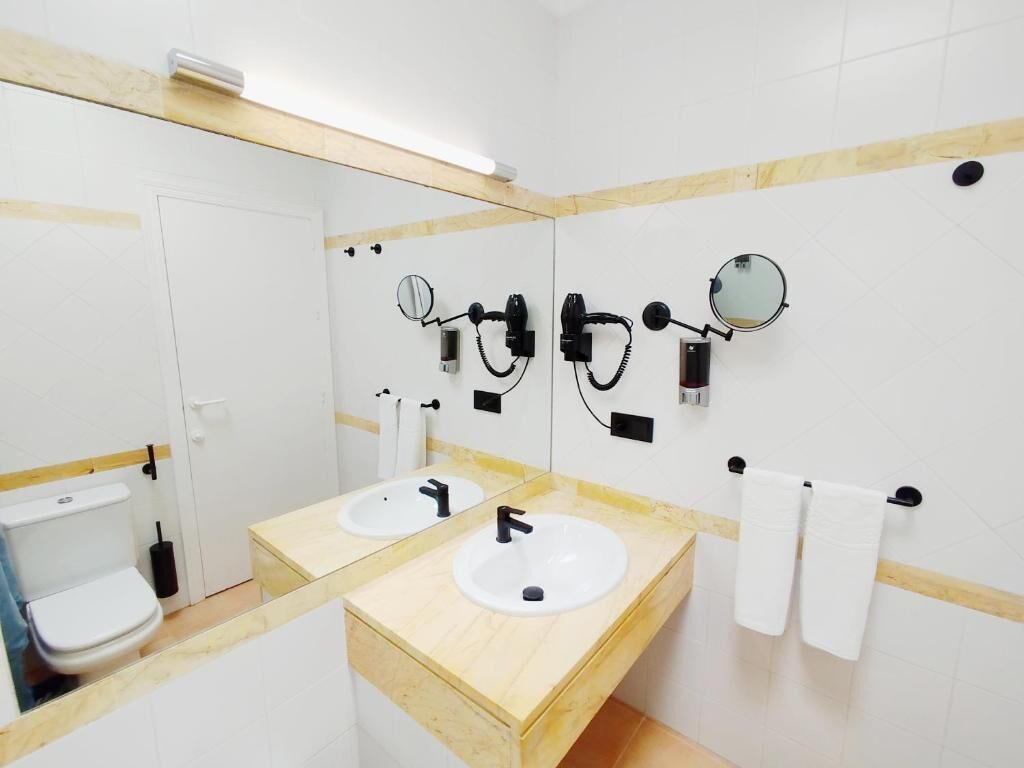 Un baño con dos lavamanos, un inodoro y un espejo.