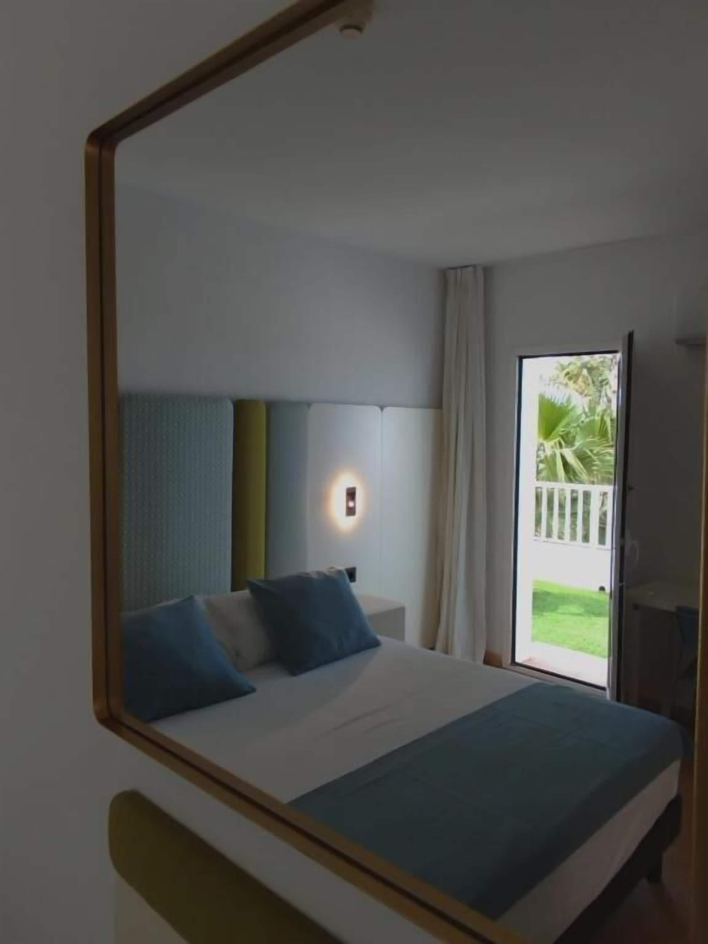 Un dormitorio con cama, mesita de noche, lámpara de pared y puerta corrediza de vidrio que da a un balcón.