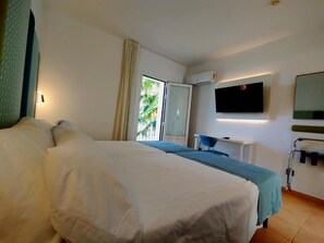 Ein Hotelzimmer mit Bett, Schreibtisch, Fernseher und einem Fenster mit Blick auf Grünflächen.