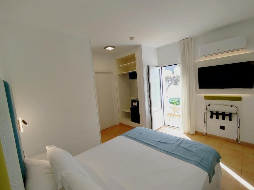 A bedroom with a bed, a wardrobe, a TV, and a sliding door to a balcony.