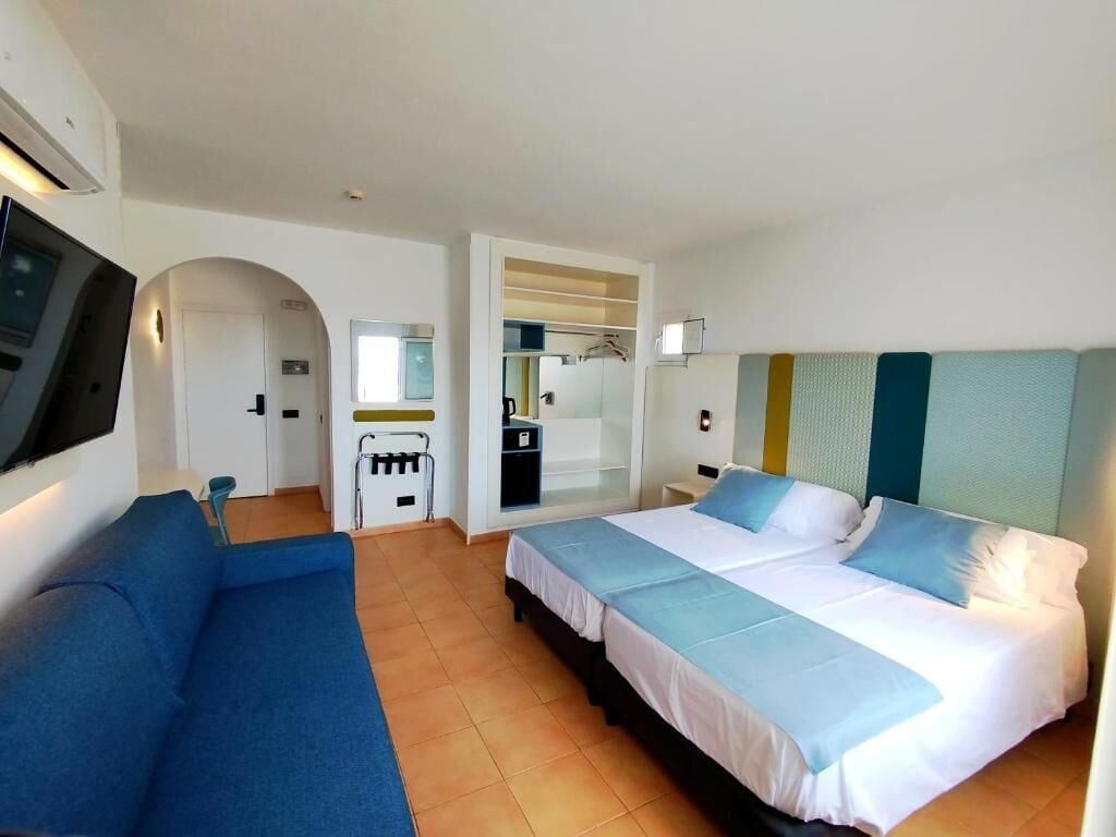 Een hotelkamer met een bed, een slaapbank, een televisie, een spiegel en een kitchenette.