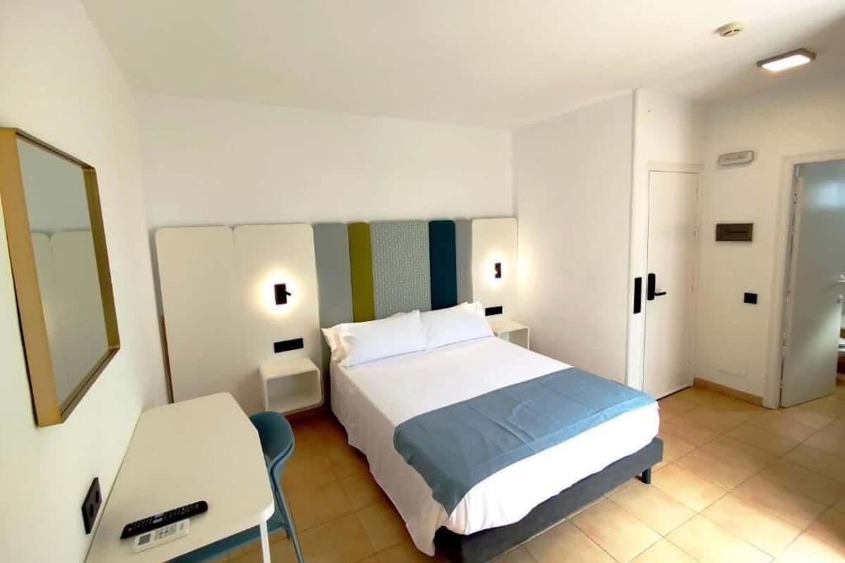 Una habitación de hotel con una cama, mesitas de noche, un escritorio y una silla.