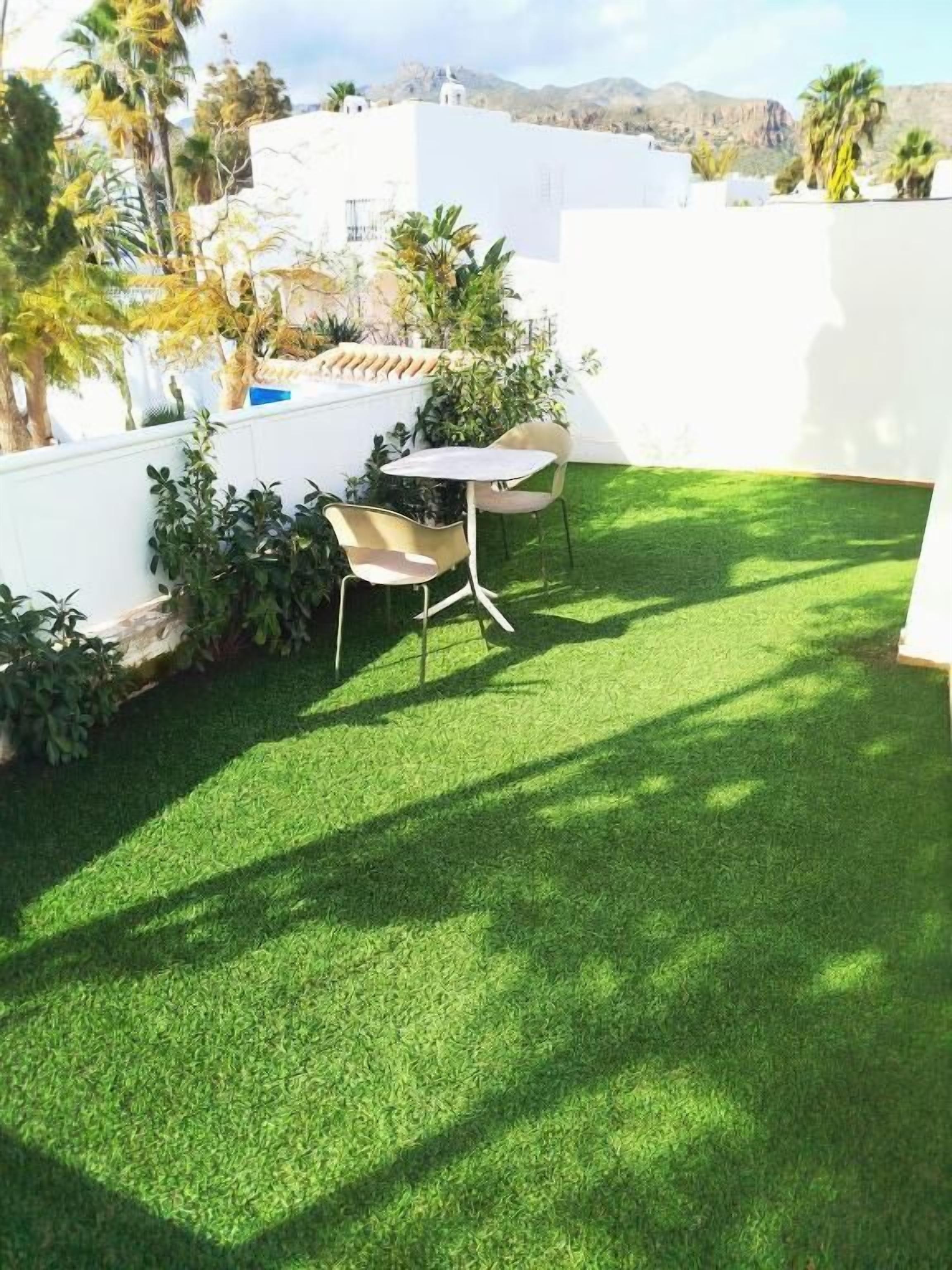 A patio with a table and chairs, surrounded by greenery and white walls.